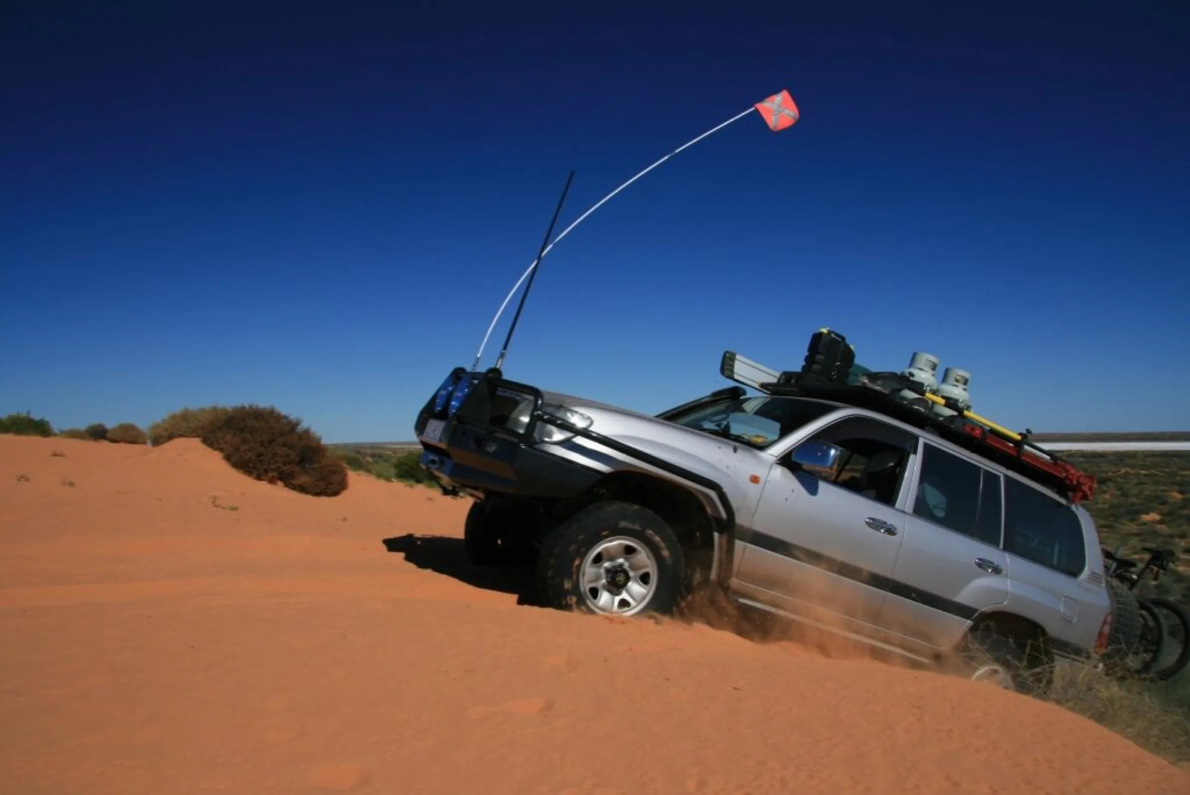 A loaded Land Cruiser climbing a red sand dune under a deep blue sky
